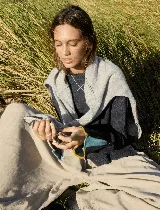 Buzo de tejido de punto color azul marino, con cuello redondo y un bordado en forma de 'X' turquesa en el pecho. La prenda se lleva con un sweater gris claro doblado sobre los hombros. La manga del buzo tiene un detalle de cierre con ribetes de colores (turquesa, amarillo y lila).