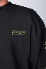 Buzo negro de corte oversize con cuello redondo y mangas largas. Presenta un pequeño logo estampado en el pecho y un diseño de empanadas y textos en la manga.
