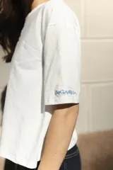 Remera blanca de algodón con cuello redondo y mangas cortas. Presenta un bordado del sol de la bandera uruguaya en el pecho.