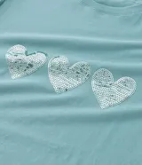 Remera de algodón color verde agua, con cuello redondo, mangas cortas abullonadas y tres corazones de lentejuelas plateadas en el frente.