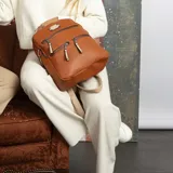 Mochila color marrón con doble apertura superior con cierres individuales, bolsillos al frente con cierres metálicos, correas largas regulables con hebillas.