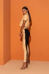 Pantalón de cuero sintético negro con corte ajustado, tiro alto y detalle de botones metálicos en el tobillo.