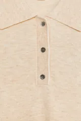 Top color crema de tejido de punto, con cuello tipo polo, manga corta y cierre frontal con botones.
