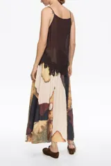 Falda midi de corte línea A con vuelo, confeccionada en poliéster. Presenta un estampado abstracto en tonos tierra, beige, marrón y verde musgo. Tiene cremallera lateral invisible y pliegues irregulares cosidos en la cintura.