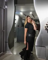 Vestido largo negro de corte ajustado, con escote asimétrico y cinturón con apliques metálicos.