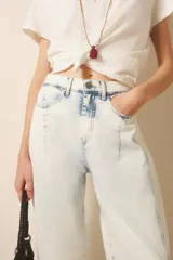 Pantalón jean de tiro medio-alto, calce holgado, relajado, con piernas anchas que se estrechan hacia el tobillo, con largo midi. Confeccionado en denim rígido con lavado bleach, que decolora el tejido hasta dejarlo casi blanco, con reservas de color en costuras y pliegues.