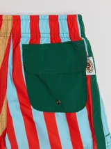 Short de baño azul con cintura elástica, rayas verdes en los laterales y bolsillo trasero con solapa roja y verde.