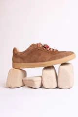 Zapatillas bajas marrones de gamuza con cordones y detalle de aplique de fresa en los cordones.