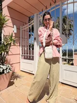 Bandolera pequeña tipo 'phone bag' de símil cuero color rosado pálido, con cierre de cremallera y correa ancha de tela con diseño de chevron en tonos claros.