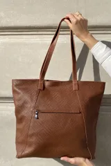 Bolso grande tipo tote de cuero color marrón con costuras decorativas en los laterales, forro interior con bolsillo para celular y bolsillo con cierre. Incluye bolsillo trasero con cierre y correas largas para colgar del hombro.
