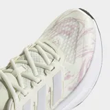 Championes de running Adidas Ultrarun 5, color crema con estampado sutil en rosado y detalles en lila. Cuentan con tres franjas blancas características de la marca y una suela gruesa blanca con base negra.