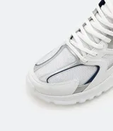 Zapatillas deportivas blancas con detalles en plateado y azul marino, de estilo chunky y suela gruesa.