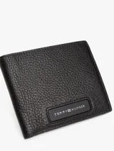 Billetera plegable Tommy Hilfiger de cuero negro con logo esmaltado en la parte delantera. Cuenta con múltiples ranuras interiores para tarjetas, compartimento para billetes, bolsillo para monedas y cinta distintiva en el interior.