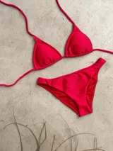Conjunto de bikini verde esmeralda con textura acanalada. El corpiño es de triángulos movibles con tiras finas para atar al cuello y a la espalda, y tiene almohadillas desmontables. La bombacha es vedetina ancha con laterales fijos.