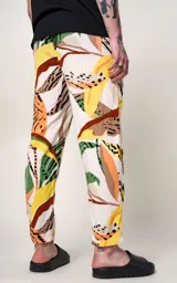 Pantalón recto de calce regular, con estampado tropical de hojas en tonos verde, naranja, amarillo y marrón sobre fondo blanco. Presenta detalles de estampado animal print en negro.