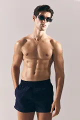 Short de baño azul marino de nylon con elástico revestido y cordón para ajustar oculto en la cintura, bolsillos laterales y bolsillo de solapa con cierre autoadherente atrás. Largo por encima de la rodilla con abertura corta en los laterales y suspensor interior en malla suave.