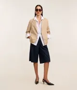 Blazer regular de sastrería color beige, con cuello solapa, sin botón, con bolsillos y detalle de pliegues en las mangas.