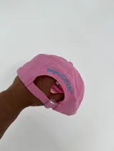 Gorro tipo béisbol color rosado con visera, bordado frontal con la palabra "AUTHENTIC" en azul y un perro dálmata en blanco y negro.