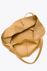 Bolso tipo shopper grande color marrón claro, confeccionado en cuero. Tiene doble asa de hombro y detalle de pespuntes en contraste. Incluye cierre con tiras y botón, y cartera con bolsillo extraíble.