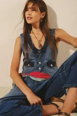 Chaleco de denim rígido azul, con efecto desgastado y detalles combinados en el tejido. Presenta cierre frontal con botones metálicos grabados, bolsillos delanteros con tapa y tira de ajuste en la espalda.