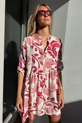 Vestido corto con estampado floral en tonos rosa y rojo. Tiene cuello mao, botones en el frente, corte con volados y mangas tres cuartos.
