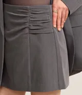 Short pollera corto color gris, de sastrería con cierre por cremallera invisible en la parte de atrás, pences y detalle en fruncido en el lateral.