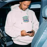 Canguro beige con capucha y bolsillo delantero tipo canguro. Estampado frontal con logo de la marca en colores verde, violeta y naranja.