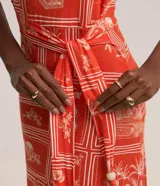 Vestido midi sin mangas confeccionado en viscosa estampada con motivos geométricos y florales en tonos naranja y blanco. Presenta escote en V, corte a la cintura con lazo y falda con volantes.