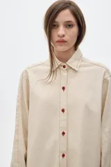 Camisa de jean color crudo, corte oversized, con botones rojos y pespuntes a contratono.
