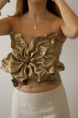 Top tipo bandeau color cobre metálico, ajustado al cuerpo, con un gran detalle floral fruncido y drapeado en el centro frontal.