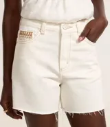 Bermuda mom de cintura mediana color blanco, confeccionada en sarga con detalle de bordado en el bolsillo reloj. Presenta trabillas en la cintura, cierre tradicional, bolsillos y costura contrastante aparente.