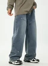 Pantalón de jean de corte relajado y ancho, color azul medio desgastado, con costuras decorativas en diagonal en la parte delantera de las piernas y bolsillos traseros.