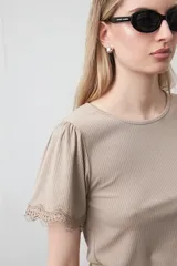 Remera de tejido acanalado color blanco, con cuello redondo y mangas cortas que presentan un detalle de terminación en puntilla en los bordes.