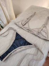 Conjunto de bikini negro con elástico tostado. El corpiño es de corte triangular con breteles regulables y aro metálico en el centro. La bombacha es tipo colaless con tiras laterales regulables.