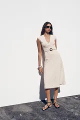 Vestido midi color crudo con jacquard floral, escote pico cruzado, manga sisa caída y cinturón ajustable con hebilla.