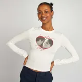 Remera blanca de manga larga con estampado frontal de los personajes Troy y Gabriella de High School Musical dentro de un corazón rojo.