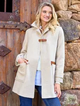 Tapado de paño de lana color crudo, con cuello alto y cierre frontal con hebilla de cuero marrón. Presenta dos bolsillos delanteros con apliques de cuero marrón.