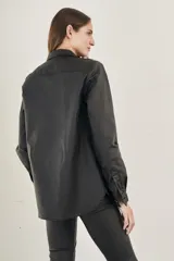 Sobrecamisa negra de textura simil cuero, con cuello camisero, cierre frontal con botones, mangas largas con puños abotonados, dos bolsillos con solapa en el pecho y corte recto.