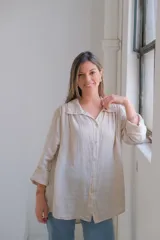 Camisa beige de lino, corte amplio, con cuello clásico, cierre frontal con botones y mangas largas con puños abotonados.