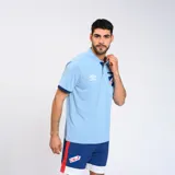 Remera polo celeste con detalles en azul marino en cuello y mangas. Escudo del Club Nacional de Football bordado en el pecho y logo de Umbro estampado en blanco.