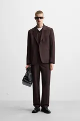 Pantalón de vestir color marrón oscuro, de corte recto, con bolsillos laterales y traseros de doble vivo. Cierre frontal con cremallera y botón.