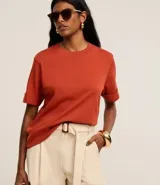 Remera de malla color naranja, de corte recto, cuello redondo y mangas cortas con dobladillo.