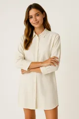 Vestido corto color crema, estilo camisa, con cuello clásico, abotonado al frente y mangas largas con puños abotonados.