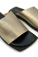 Sandalia de cuero color oro con diseño minimalista y suela negra.