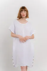 Vestido corto color beige confeccionado en lino, de corte recto y calce holgado. Presenta botones decorativos en los laterales y bolsillos laterales.