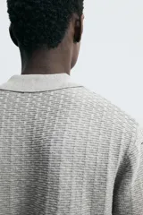Polo gris de punto con textura, corte regular, cuello solapa y cierre frontal con botones.