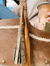Bolso matero de cuero color marrón con divisiones internas para transportar termo, mate y yerba. Tiene manija trenzada y flecos decorativos.