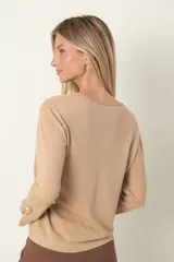 Buzo color beige de punto, con cuello redondo y puños abiertos decorados con moña y perla.