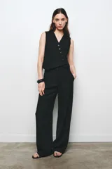 Chaleco negro de Zara Woman Collection, con escote pico y sin mangas. Presenta falsos bolsillos de vivo en el delantero, bajo asimétrico y cierre frontal cruzado con botones.