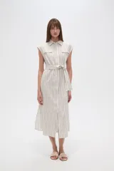 Vestido camisero midi sin mangas, con cuello camisero, cierre frontal con botones, bolsillos en el pecho, cinturón de tela con lazo y estampado a rayas verticales en tonos beige y blanco.